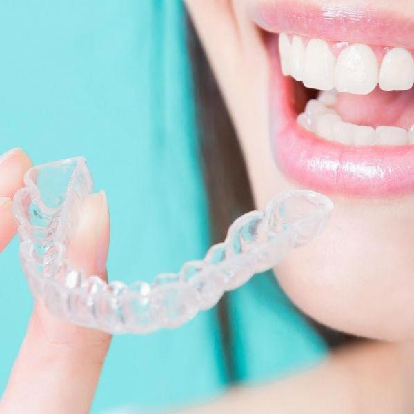 Woman smiling showing her white teeth holding clear invisalign