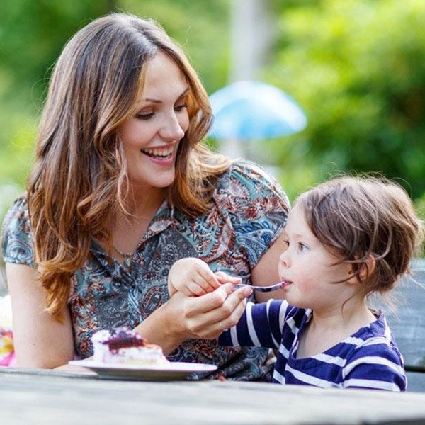 Mother feeding her daughter cake at the park