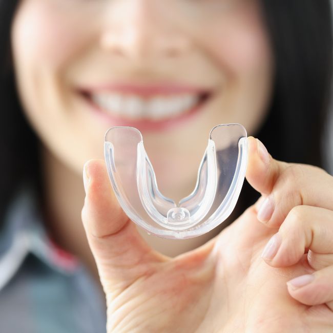 Woman smiling showing her white teeth holding a mouth guard