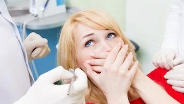 woman at clinic hiding her mouth due to fear of dental doctor